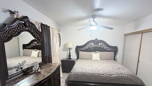 Ein Schlafzimmer mit einem großen Bett, einer Kommode, einem Nachttisch, einem Deckenventilator und einem Spiegel.