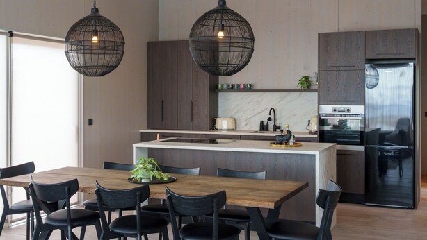 A modern kitchen with a central island, dark wooden cabinets, stainless steel appliances, and black pendant lighting.