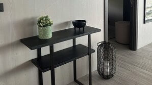 A modern interior with a round mirror, a black console table, a potted plant, a black bowl, and a wicker basket.