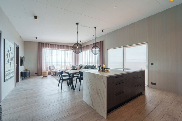 A modern kitchen with a central island, dining area with chairs, and a large window. - Design House in Akureyri – Private Hot Tub, Sea & Mountain Views, 2 bathrooms (Akureyri)