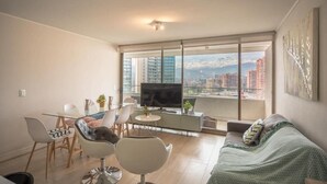 Un salon moderne comprenant un coin repas, un téléviseur à écran plat et une grande fenêtre donnant sur la ville.