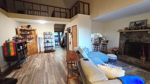 A spacious living room with a high ceiling, a fireplace, a staircase, and a kitchen area. - Delightful 2-bedroom cabin in charming Zionville awaits you. (Zionville)