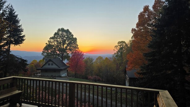 A house with a deck, surrounded by trees and a view of the sunset. - Delightful 2-bedroom cabin in charming Zionville awaits you. (Zionville)