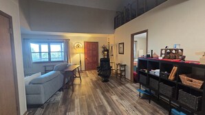 A living room with a sofa, a chair, a wooden floor, a bookshelf, and a door. - Delightful 2-bedroom cabin in charming Zionville awaits you. (Zionville)