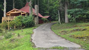 A cabin with a stone chimney, a wooden deck, and a gravel path leading to it. - Delightful 2-bedroom cabin in charming Zionville awaits you. (Zionville)