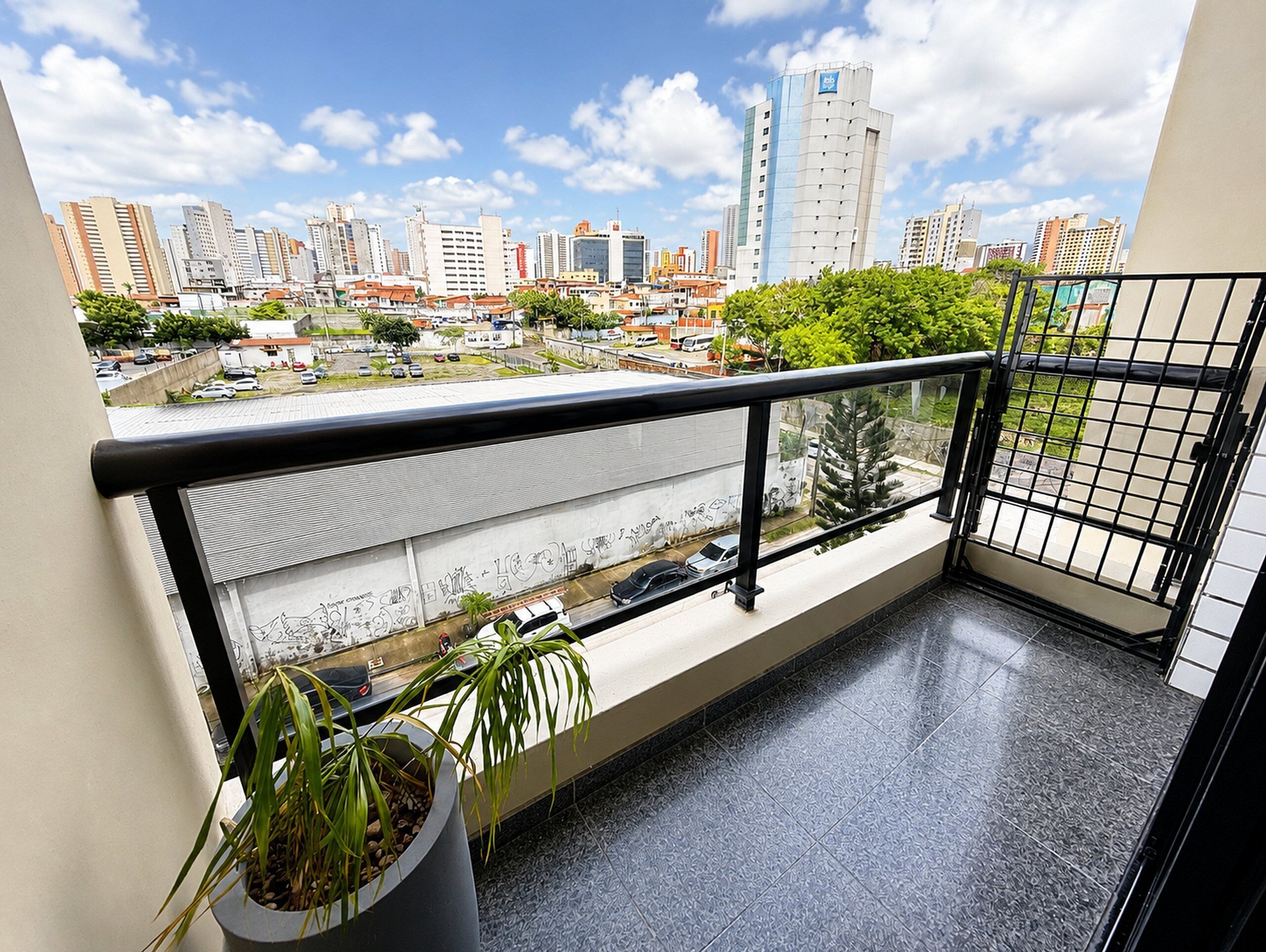 Un balcon agrémenté d’un pot de fleurs, avec vue sur un paysage urbain composé d’immeubles et d’un ciel dégagé.