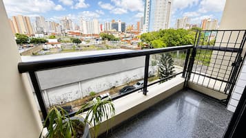 A balcony with a potted plant, a view of a cityscape with buildings and a clear sky.