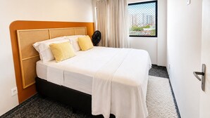 Et hotelværelse med seng, et vindue med gardiner, en ventilator og udsigt til bygninger.