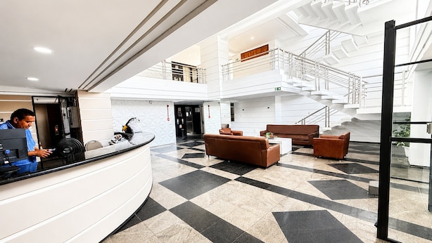 Et hotellobby med receptionsdisk, siddeområde og en trappe til et øvre niveau.
