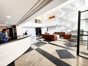 A hotel lobby with a reception desk, seating area, and a staircase leading to an upper level. - Hosts BR - Ap. com Rooftop Vista Mar (Fortaleza)
