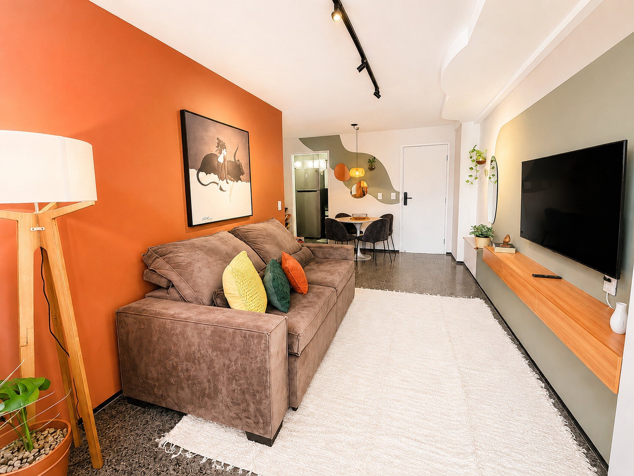 Uma sala de estar moderna com um sofá, uma televisão de tela plana e um espaço de refeições ao fundo.