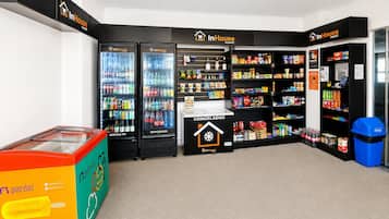 A self-service kiosk with refrigerated and frozen beverages, snacks, and a trash bin.