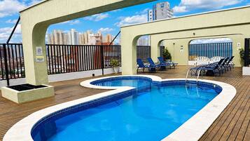 Piscina no terraço com vista para o horizonte da cidade, espreguiçadeiras e um deck de madeira.