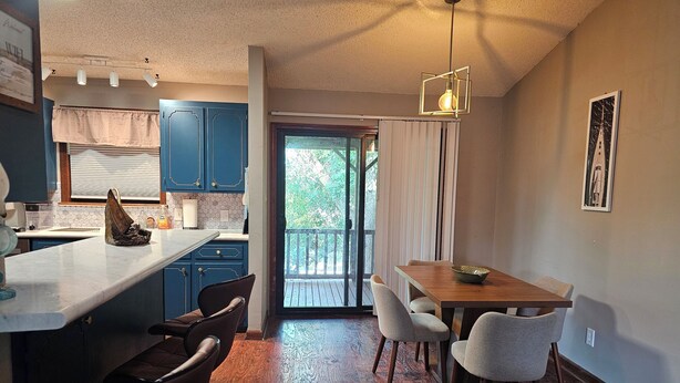 A modern kitchen with blue cabinets, a wooden dining table, and a view to the outside.