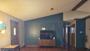 A living room with a wooden floor, a television on a wooden stand, and a door with a light fixture.