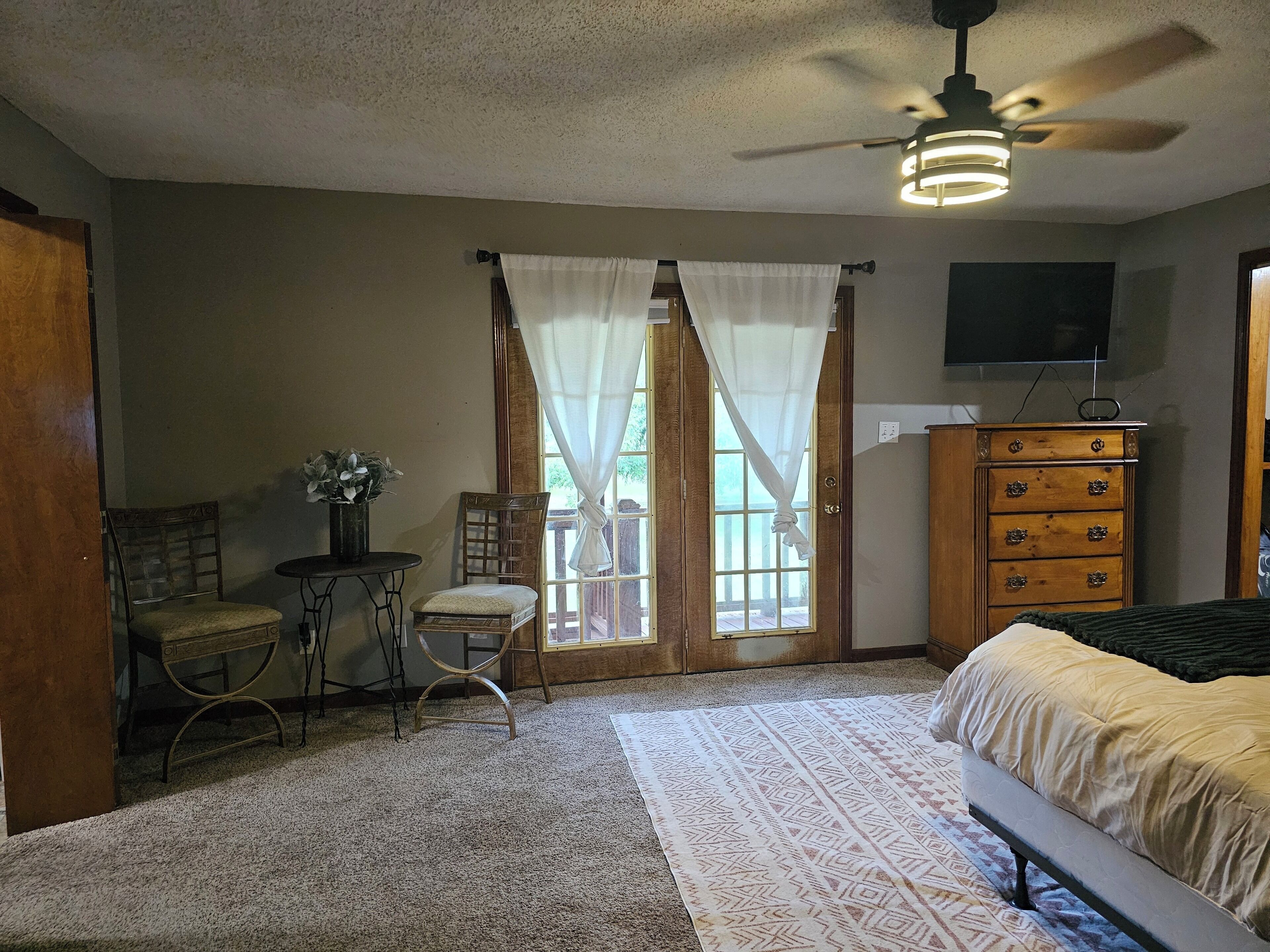 Une chambre à coucher comprenant un lit, une commode, une chaise, une petite table avec une plante et un ventilateur de plafond.