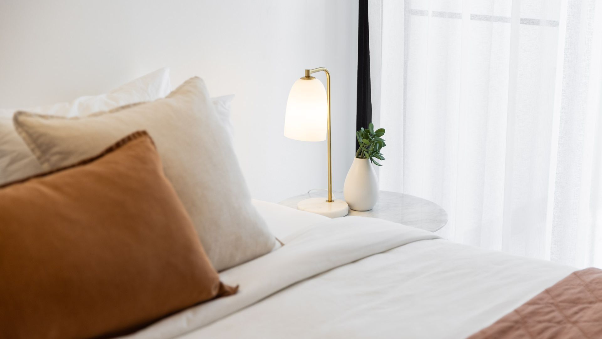 A neatly made bed with pillows, a bedside lamp, and a potted plant on a bedside table.