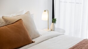 Ein ordentlich bezogenes Bett mit Kissen, einer Nachttischlampe und einem Blumentopf auf einem Nachttisch.