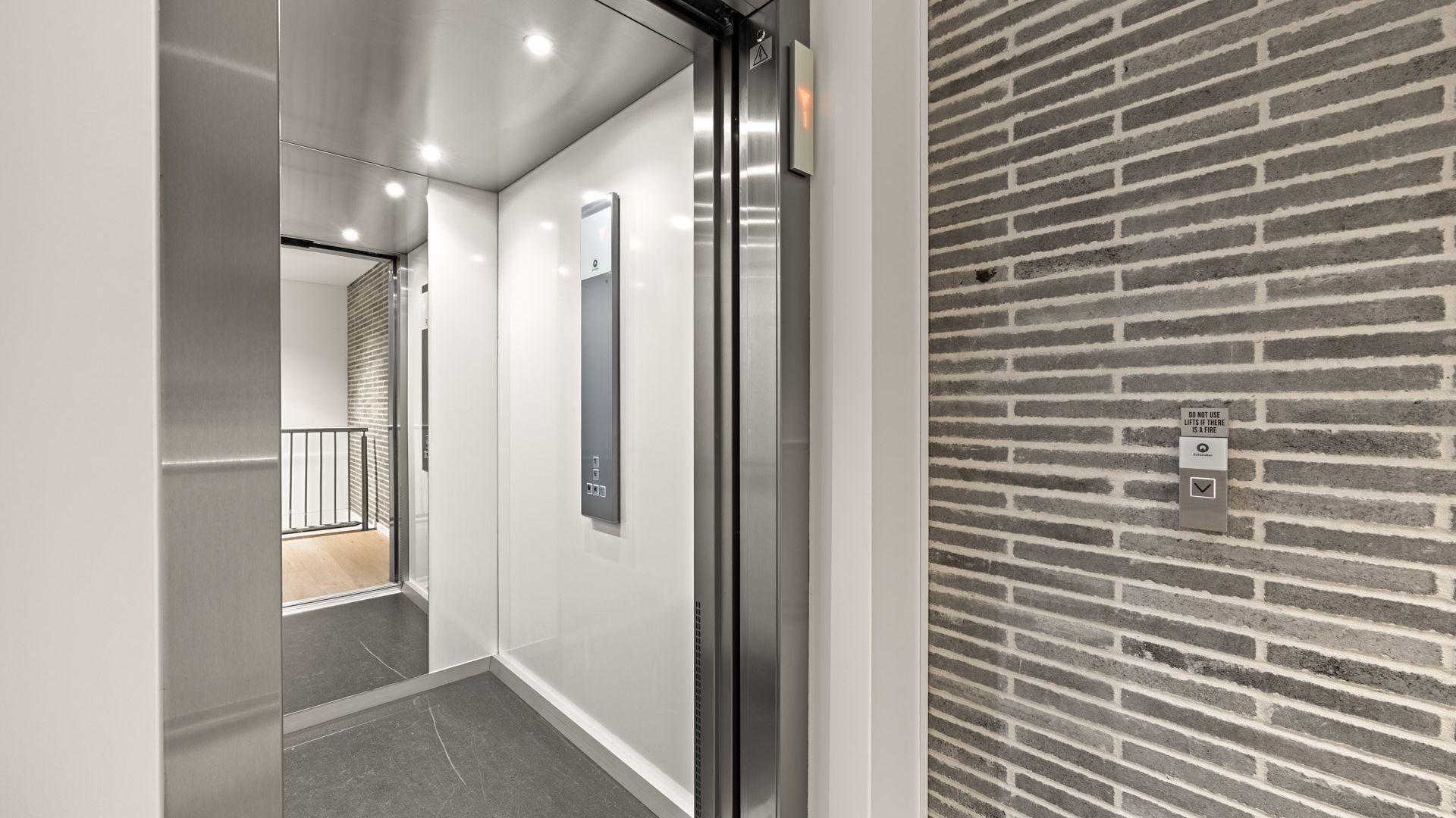 A modern elevator with a glass door and a wall-mounted control panel.