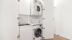 A compact laundry room with a washing machine, a sink, and a basket. - The Avenue ~ Sawtell Village Prime Location (Sawtell)