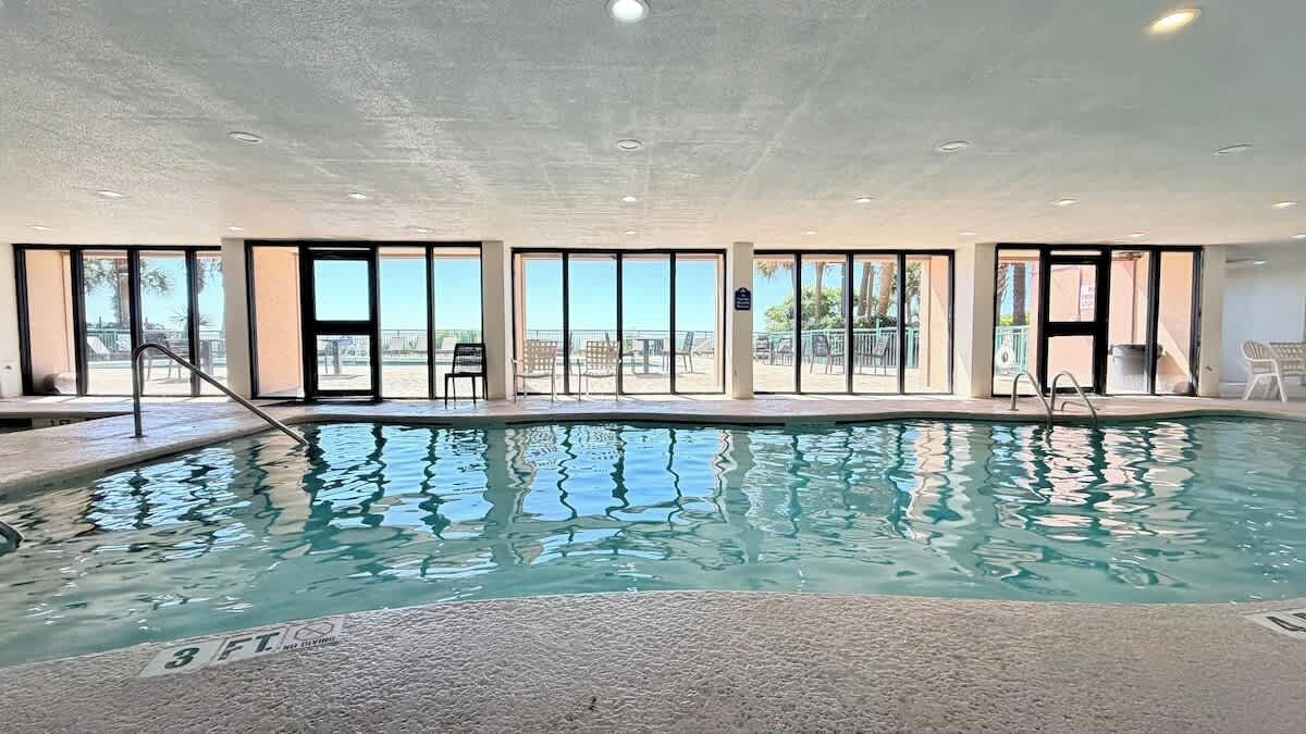 Una piscina interior con paredes de vidrio transparente, una marca de profundidad de 90 centímetros y vistas a la playa.