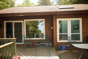 Eine Holzterrasse mit Metallstühlen und einem Tisch, eine Schiebeglastür und ein Fenster mit einer Pendelleuchte.