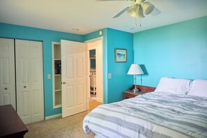 Ein Schlafzimmer mit einem Bett, einem Nachttisch, einer Lampe, einem Deckenventilator und einer Tür zu einem Kleiderschrank.