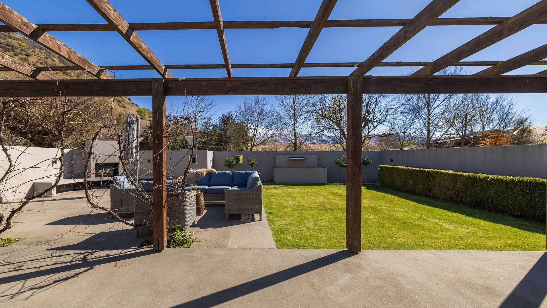 Un patio couvert avec une pelouse, du mobilier d’extérieur et une structure en forme de pergola.