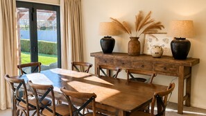 A dining area with a wooden table and chairs, a sideboard with decorative items, and a view through a glass door. - Thirty-One on Ferry - away from home in beautiful Queenstown (Queenstown)