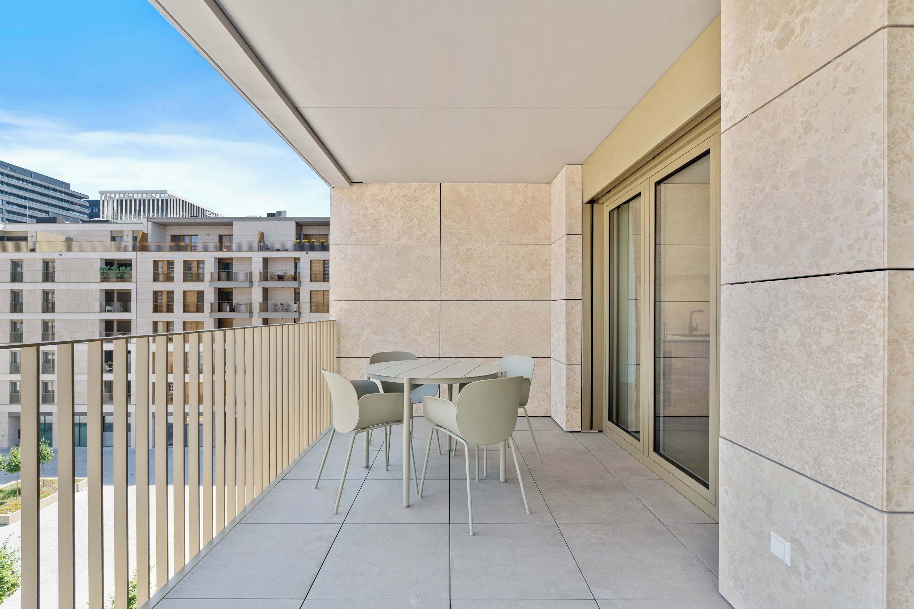 A balcony with a table and chairs, a sliding glass door, and a view of other buildings.