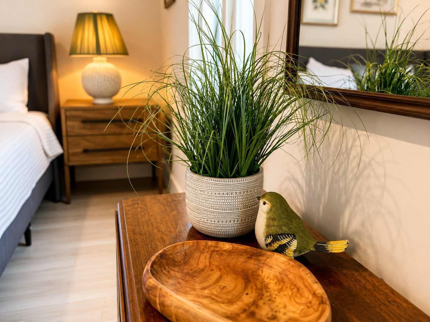 Une table de chevet en bois ornée d’un bol décoratif, d’une plante en pot et d’une figurine d’oiseau.