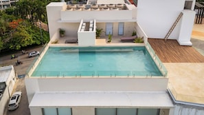 A rooftop pool with a view of the street below, surrounded by greenery and a building with multiple floors. - Stylish Apartment | Rooftop Pool & King Bed (Cancún)