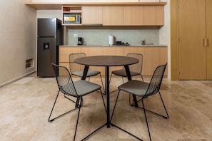 A compact kitchen with a round table and four chairs, a refrigerator, and wooden cabinets. - Stylish Apartment | Rooftop Pool & King Bed (Cancún)