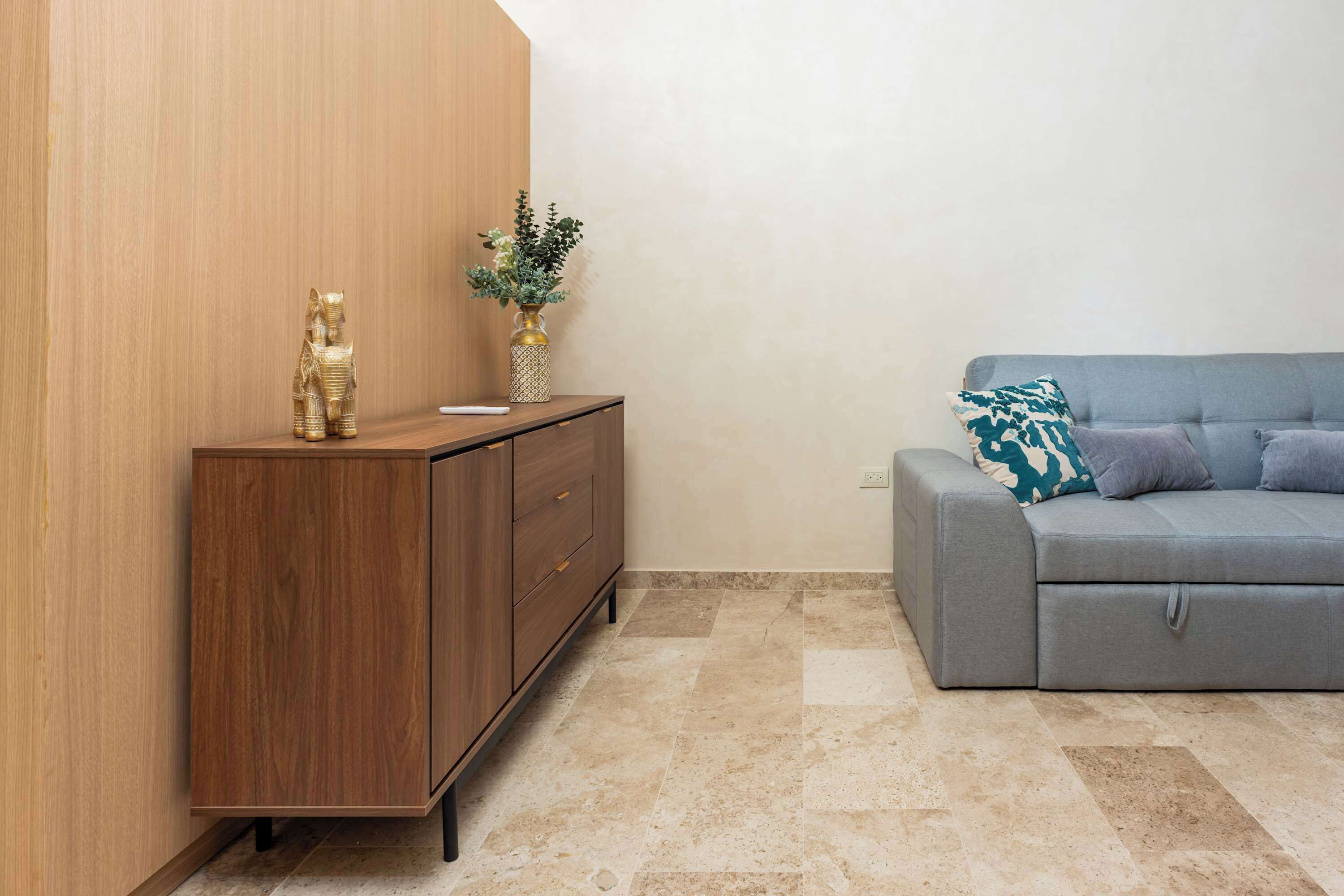 Een moderne woonkamer met een grijze bank, een houten kast en een vaas met bloemen.