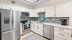 Una cocina moderna con electrodomésticos de acero inoxidable, armarios blancos, salpicadero de azulejos y lavavajillas integrado.