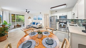Una cocina moderna con electrodomésticos de acero inoxidable, un comedor con una mesa redonda y una sala de estar con un sofá y obras de arte.