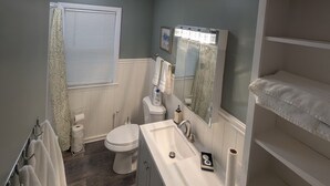 Et badeværelse med toilet, vask, spejl og et håndklædetørrestativ.