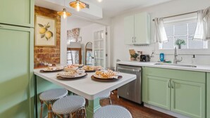 Een keuken met een centraal eiland, groene kastjes, een raam met gordijnen en een hanglamp.