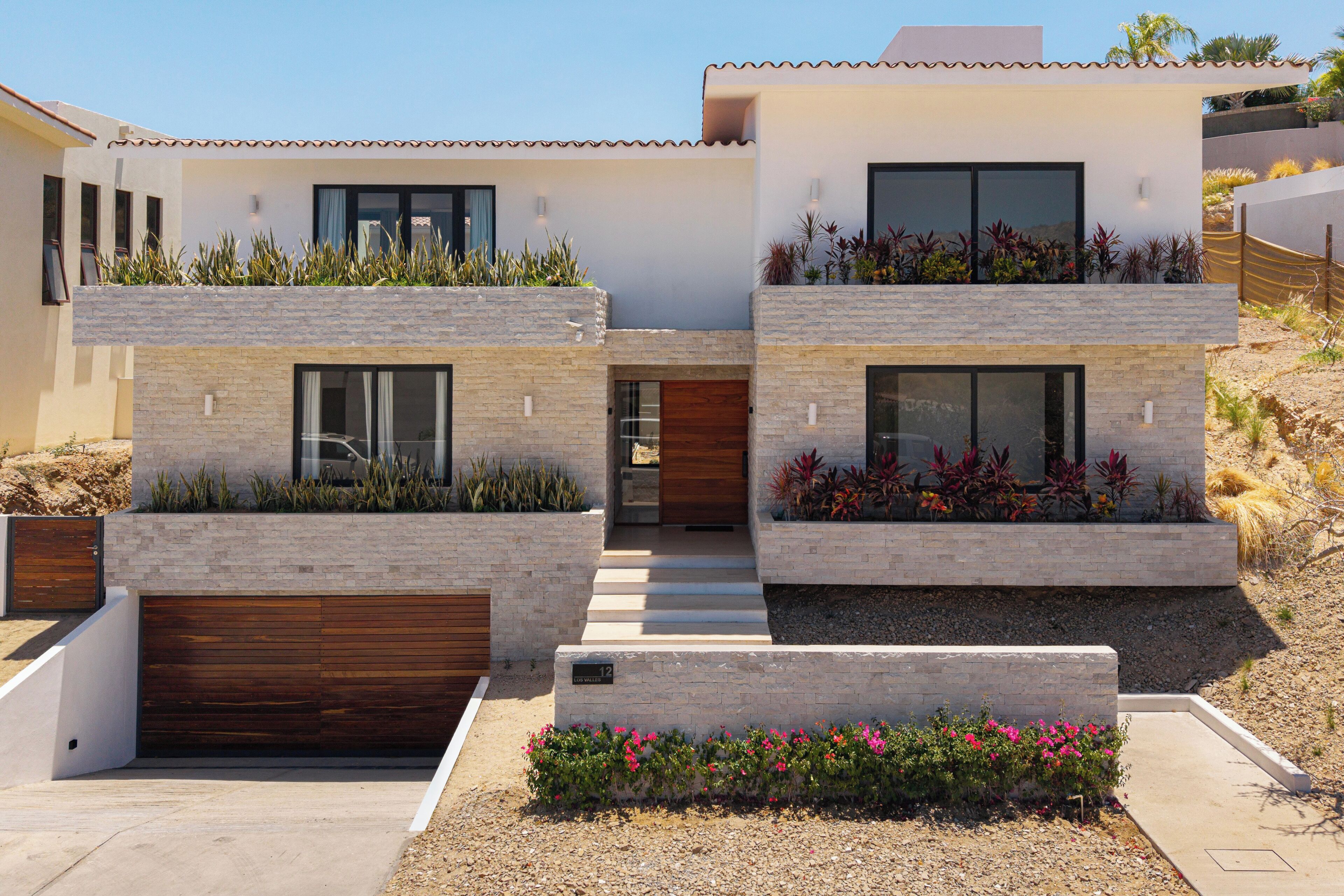 Une maison moderne à deux étages, dotée d’un toit plat, de grandes fenêtres et d’une façade en pierre.