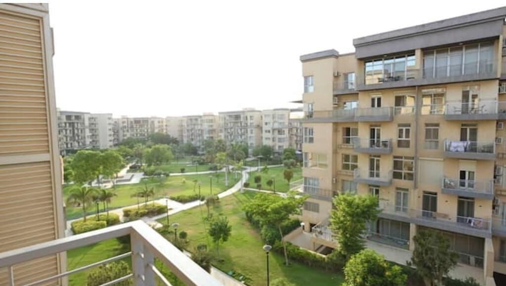 Un immeuble résidentiel doté de nombreux balcons, d’une cour verdoyante et d’un ciel dégagé.