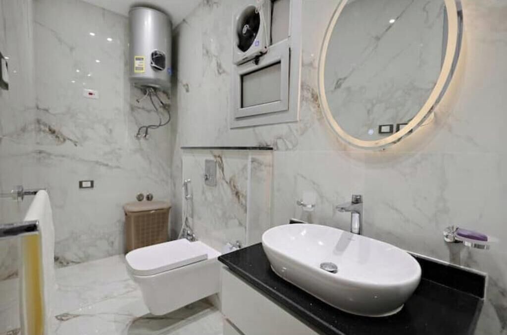 Ein modernes Badezimmer mit Marmorboden, einer freistehenden Toilette, einem Waschbecken mit Waschtisch, einem Handtuchhalter und einem wandmontierten Spiegel.