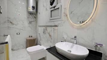 Ein modernes Badezimmer mit Marmorboden, einer freistehenden Toilette, einem Waschbecken mit Waschtisch, einem Handtuchhalter und einem wandmontierten Spiegel.