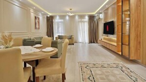 A modern living room with a dining area, a TV mounted on a wooden wall, and a large window with curtains.