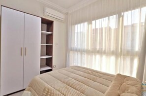 Um quarto com cama, guarda-roupa e janela com cortinas.