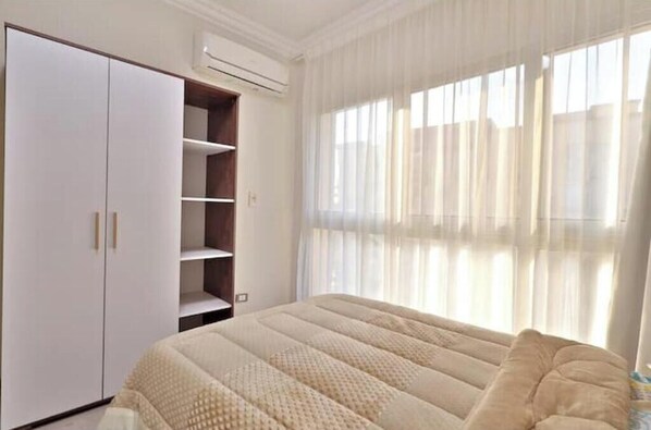 A bedroom with a bed, a wardrobe, and a window with curtains.