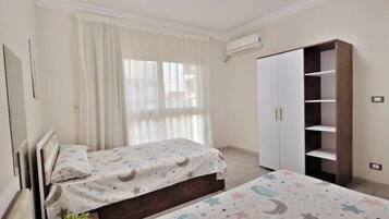 Quarto com duas camas, um guarda-roupa e uma janela com cortinas.