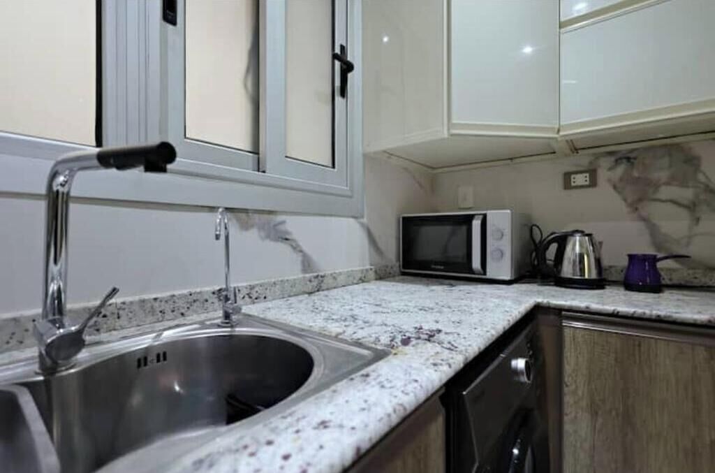 A kitchen with a stainless steel sink, a microwave, and a kettle on the countertop.