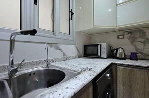 A kitchen with a stainless steel sink, a microwave, and a kettle on the countertop.