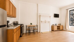 A modern kitchen with wooden cabinets, a granite countertop, a built-in stove, and a dining area with a table and chairs. - Bright Uptown Manhattan Studio Near Subway and Dining (New York)