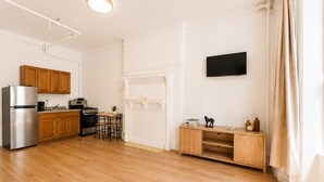 A modern kitchen with wooden cabinets, a stainless steel refrigerator, a stove, and a dining area with a table and chairs. - Bright Uptown Manhattan Studio Near Subway and Dining (New York)